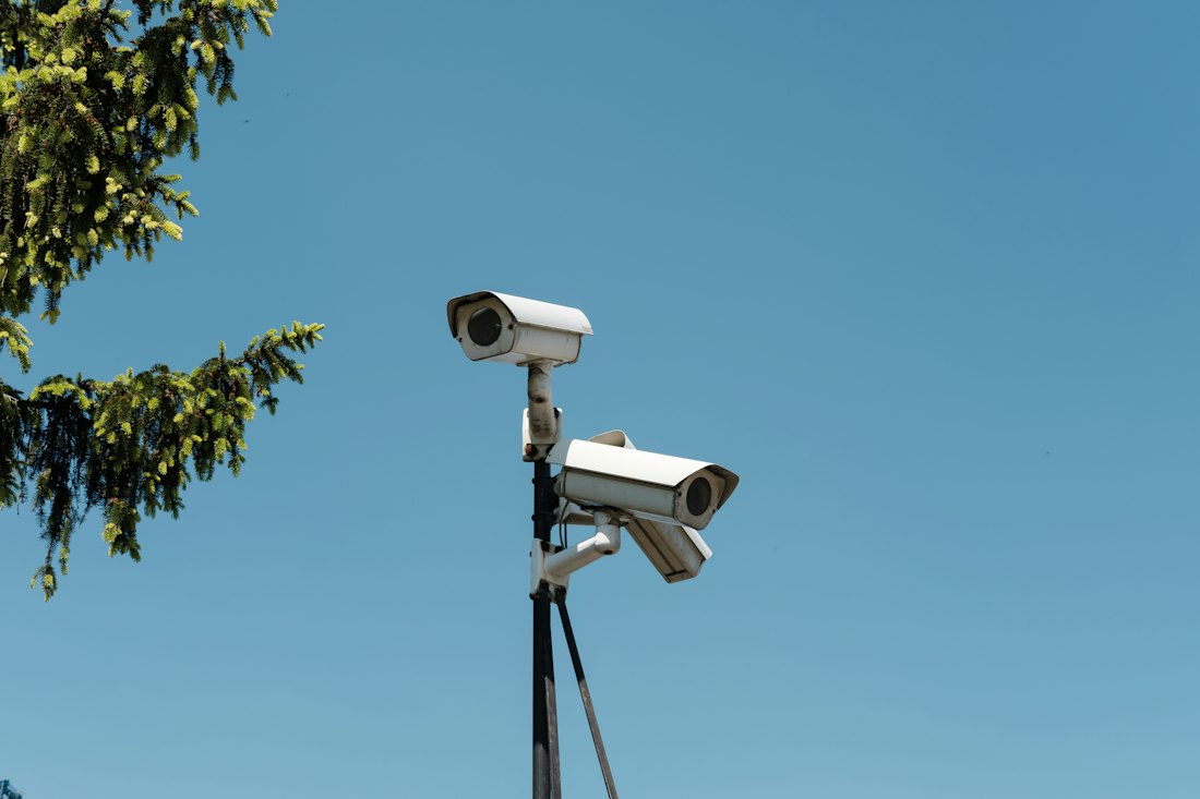 Two security cameras mounted on a pole against a blue sky